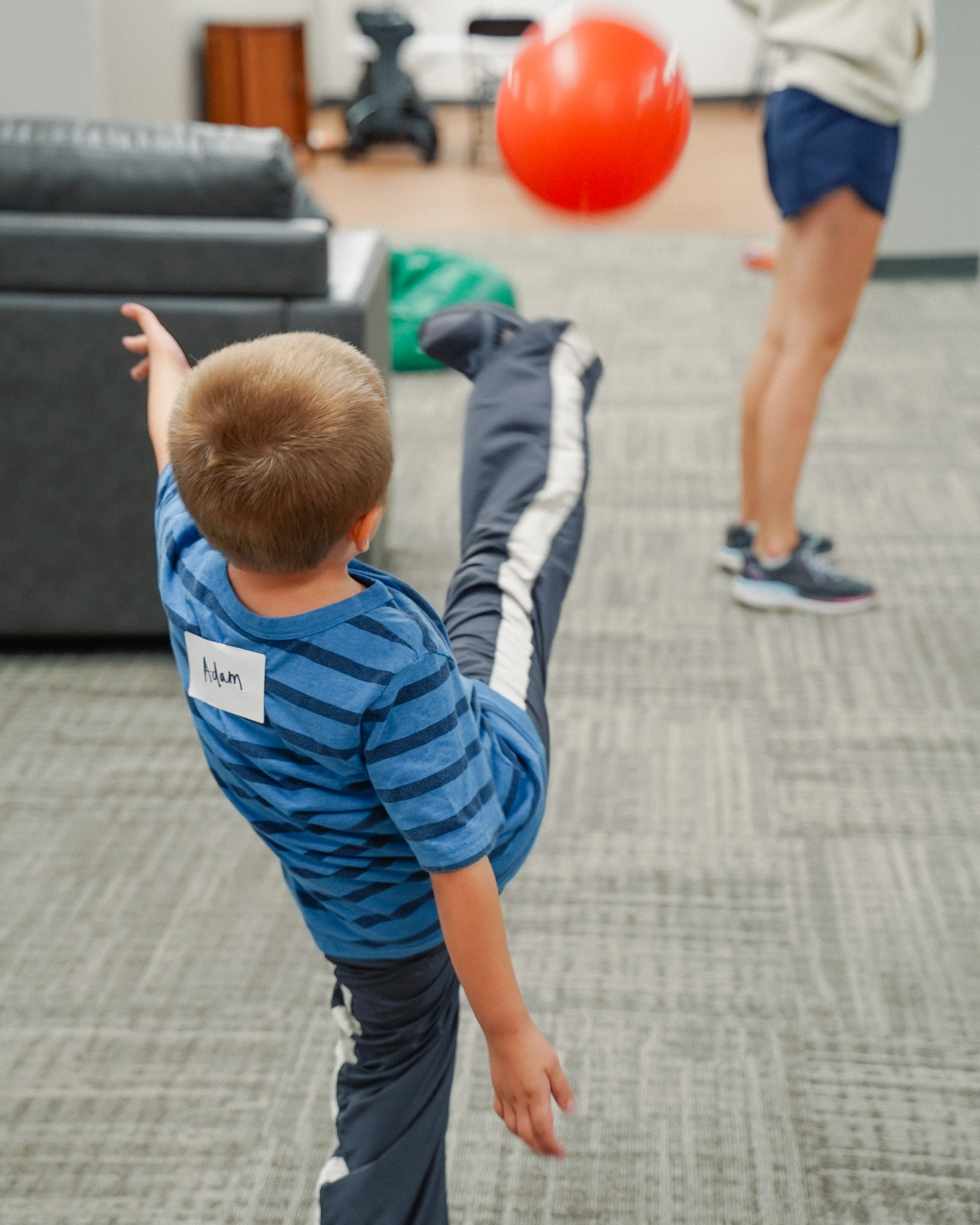 A young boy kicks a red ball high into the air inside a room