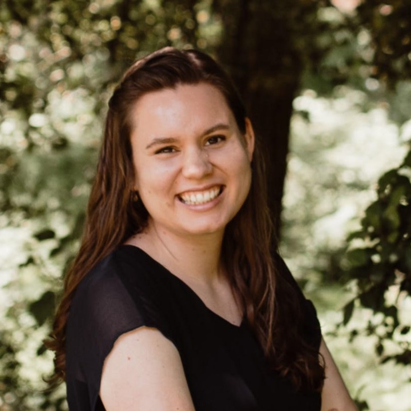 Headshot of a woman smiling at the camera with trees in the background.